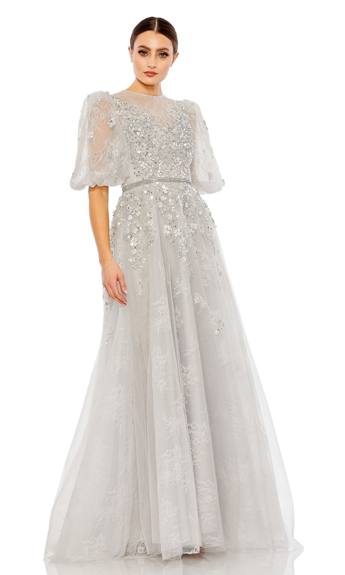 A woman wears the Long Formal Dress 20445 by Mac Duggal, a light grey lace ball gown with floral embellishments, sheer puff sleeves, and a floor-length sheer overlay.
